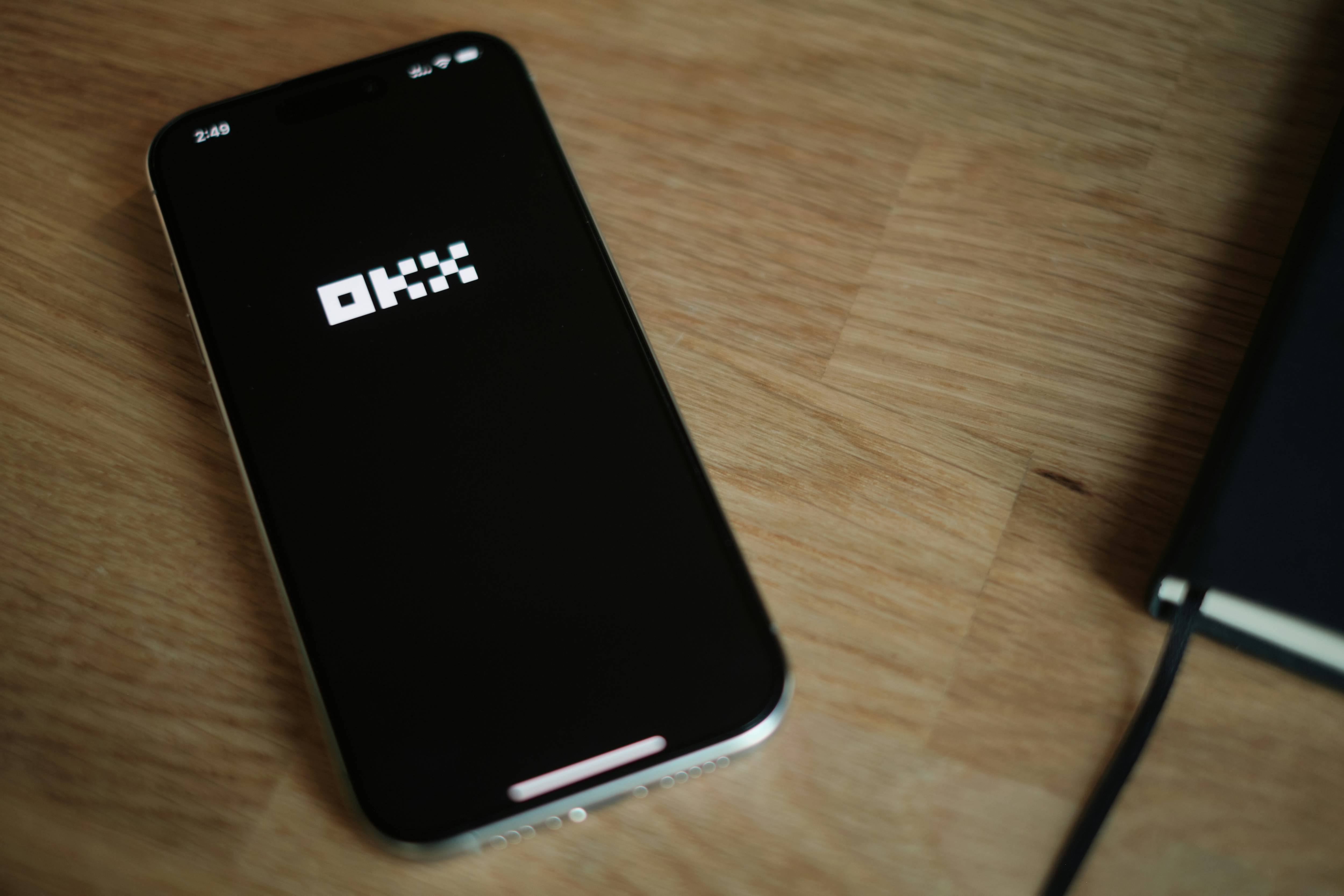Smartphone displaying OKX logo on wooden table.