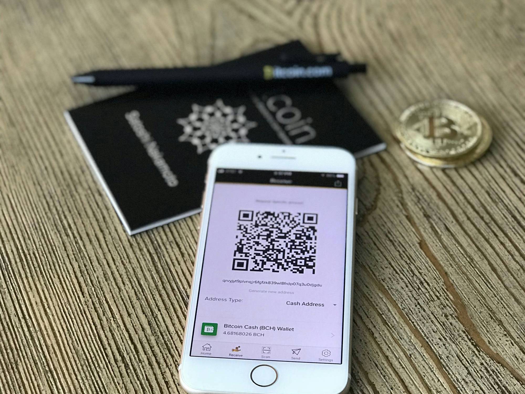 Smartphone displaying QR code next to Bitcoin on wooden table.