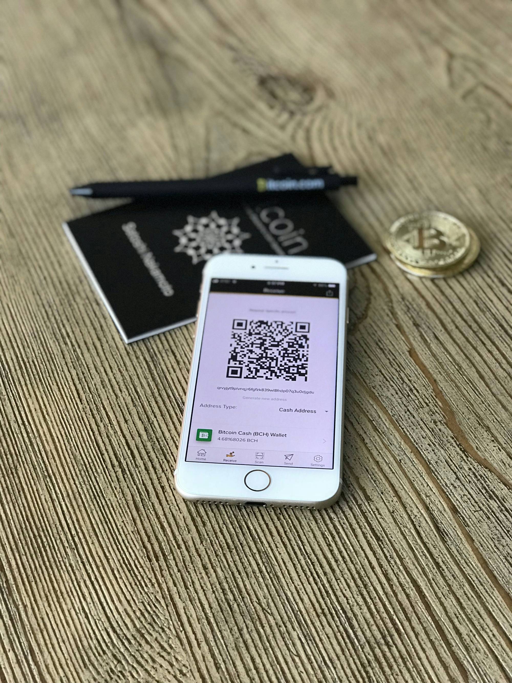 Smartphone displaying QR code next to Bitcoin on wooden table.