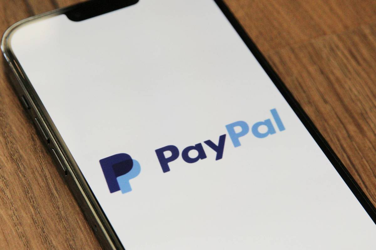 Smartphone on wooden table displays the PayPal logo.