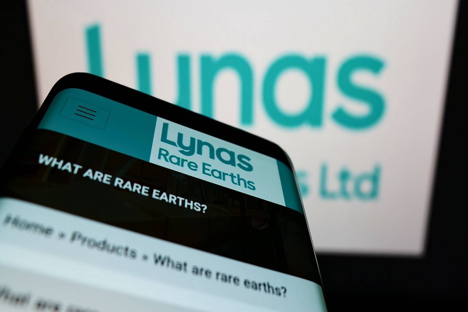 Smartphone showing Lynas Rare Earths website, logo blurred in background.