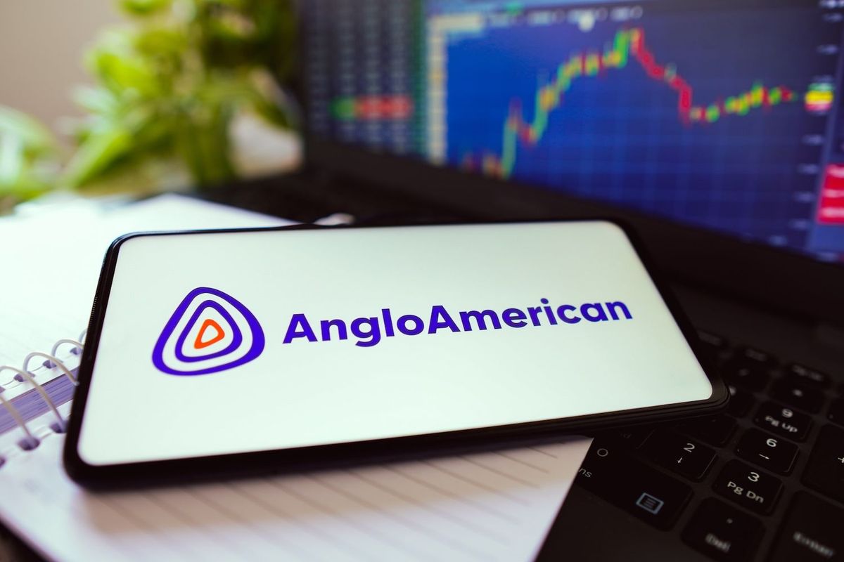 Smartphone with Anglo American logo on screen in front of a laptop showing a stock chart.