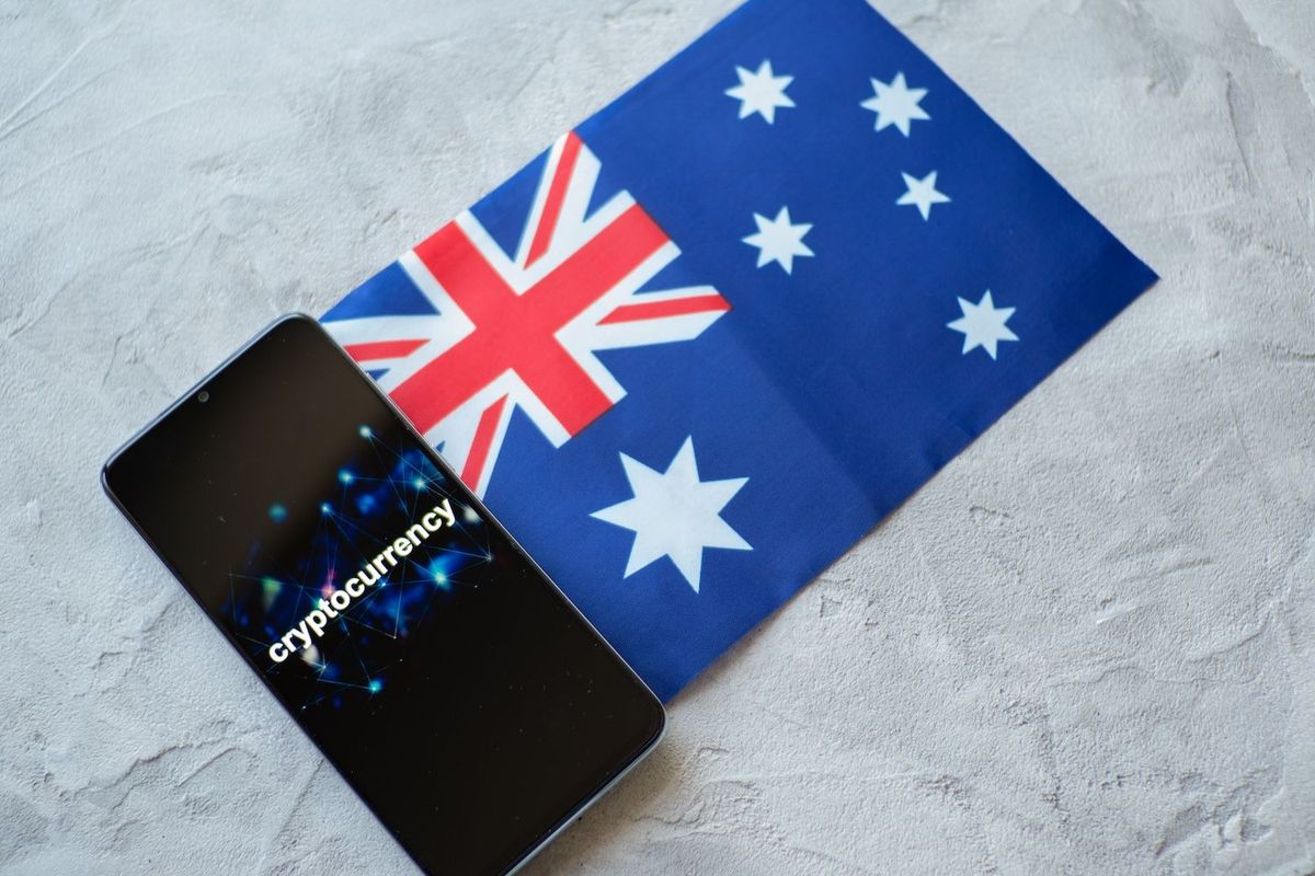 Smartphone with "cryptocurrency" text beside Australian flag on a textured surface.