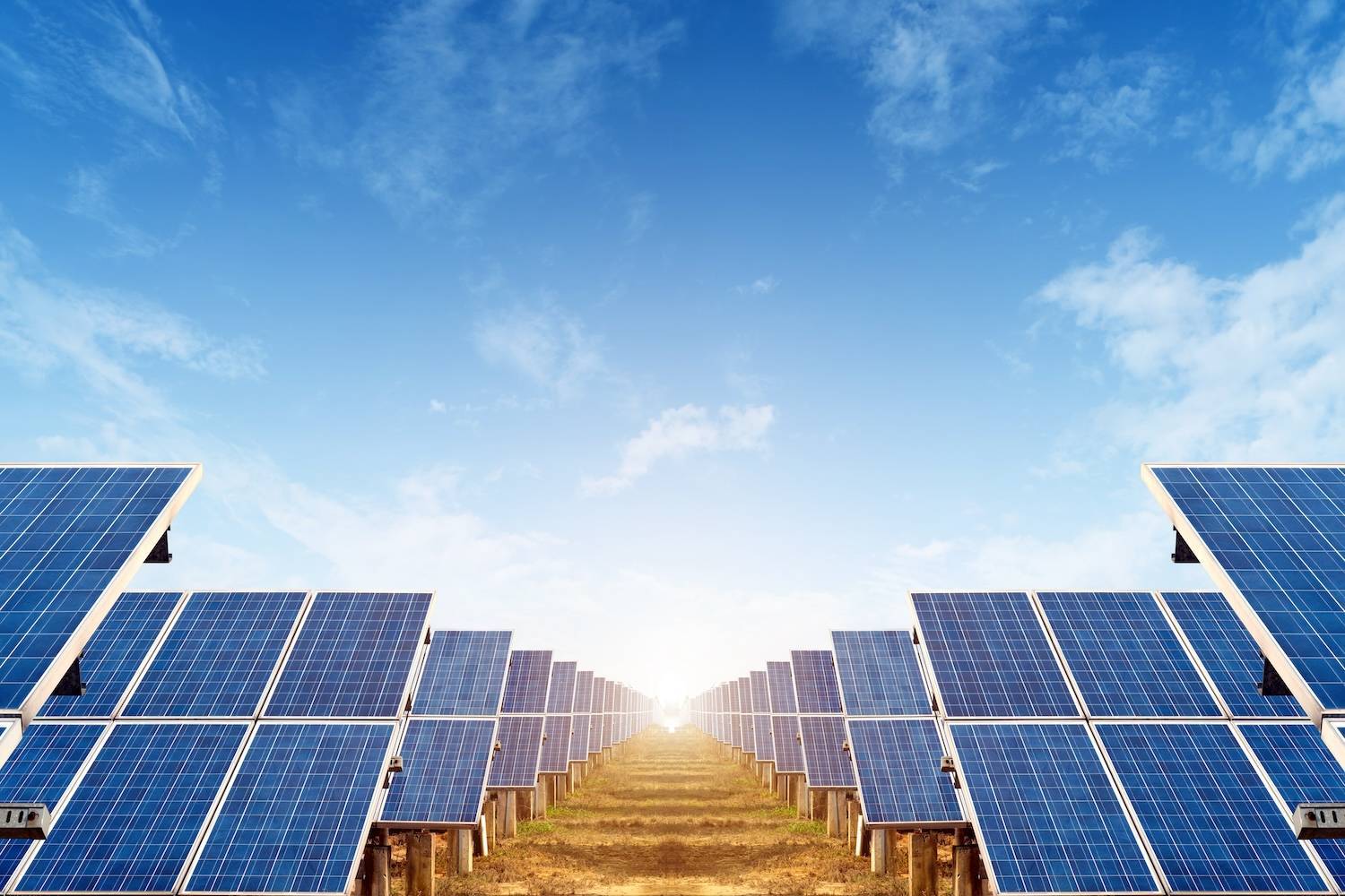 Solar panels aligned under a clear blue sky, capturing sunlight in a vast open field.