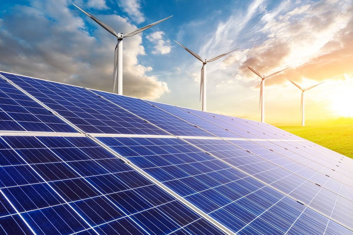Solar panels and wind turbines under a bright sky at sunset.