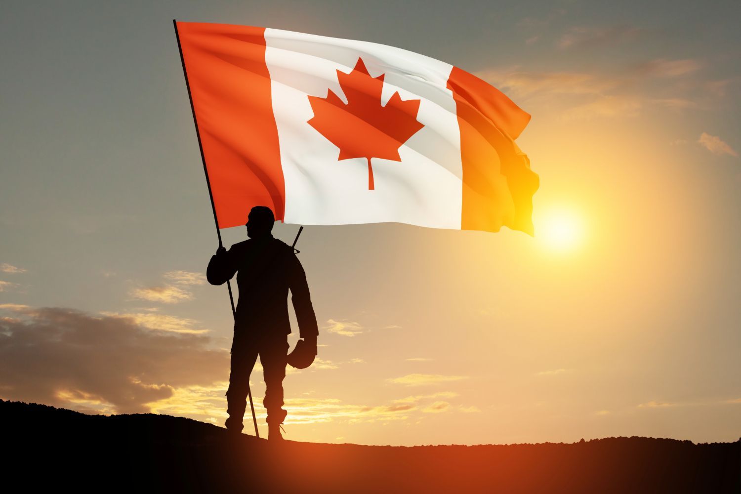 Soldier holding a Canadian flag at sunset.