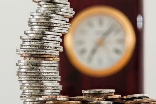 stack of coins in the foreground with a clock in the background