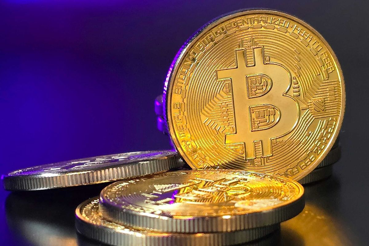 Stack of shiny gold Bitcoins on a reflective surface with a purple background.