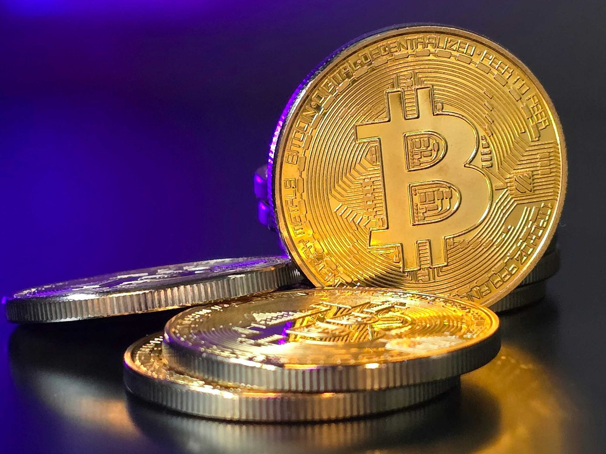 Stack of shiny gold Bitcoins on a reflective surface with a purple background.