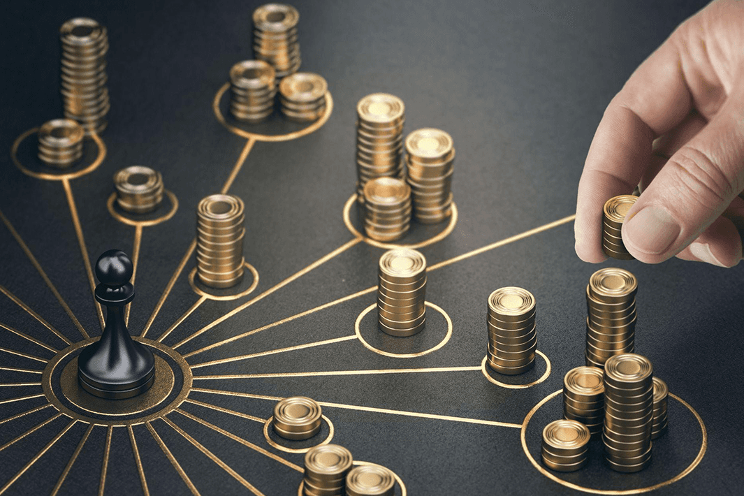 Stacks of gold coins on black diagram with a hand arranging and a black game piece central.