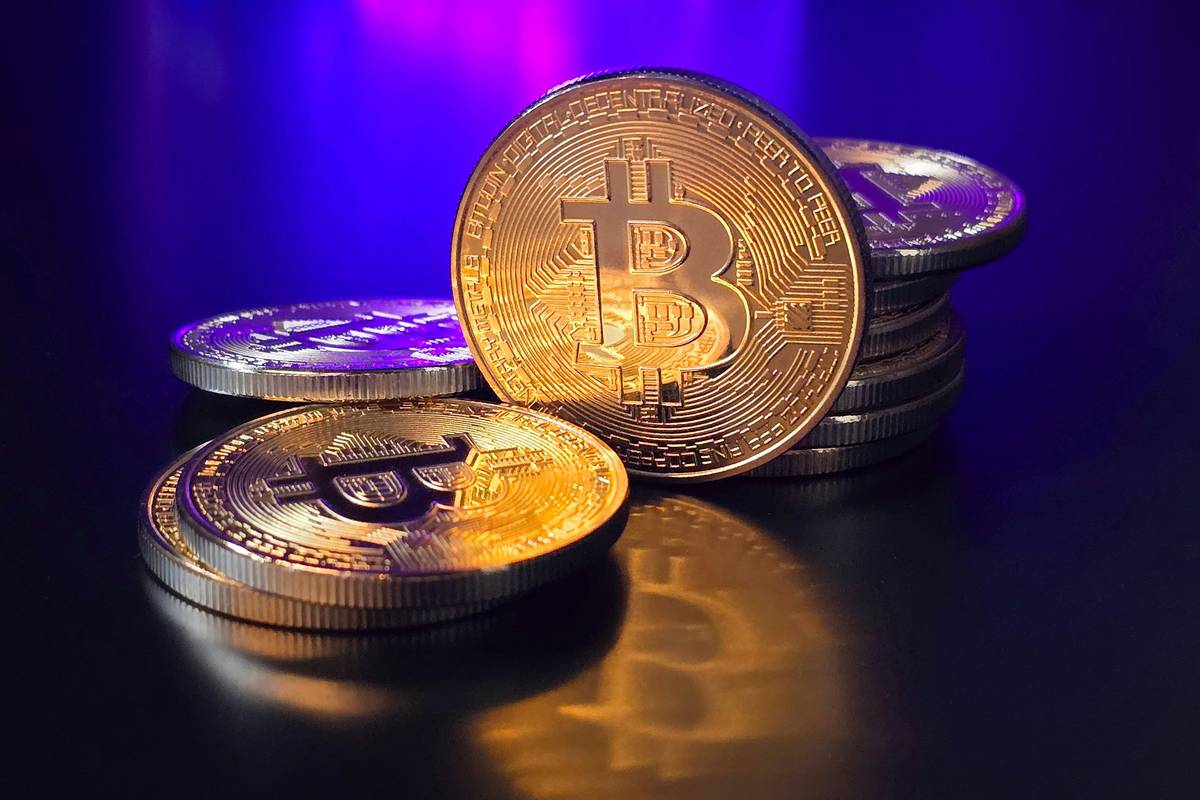 Stacks of shiny gold Bitcoin coins on a reflective surface with a blue glow.