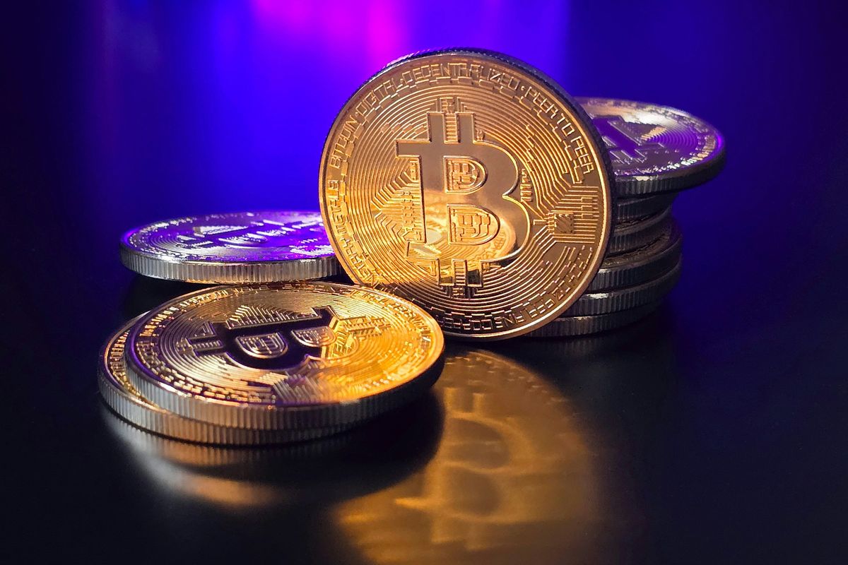 Stacks of shiny gold Bitcoin coins on a reflective surface with a blue glow.