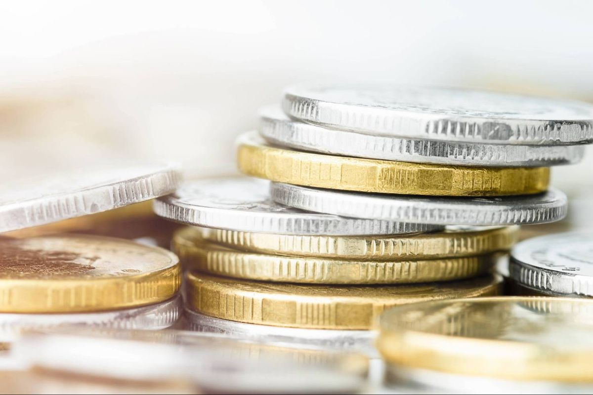 Stacks of silver and gold coins piled on a white surface, with a blurred background.