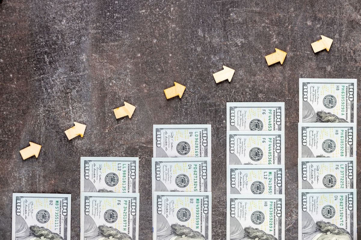 Stacks of US$100 bills with upward-pointing wooden arrows.