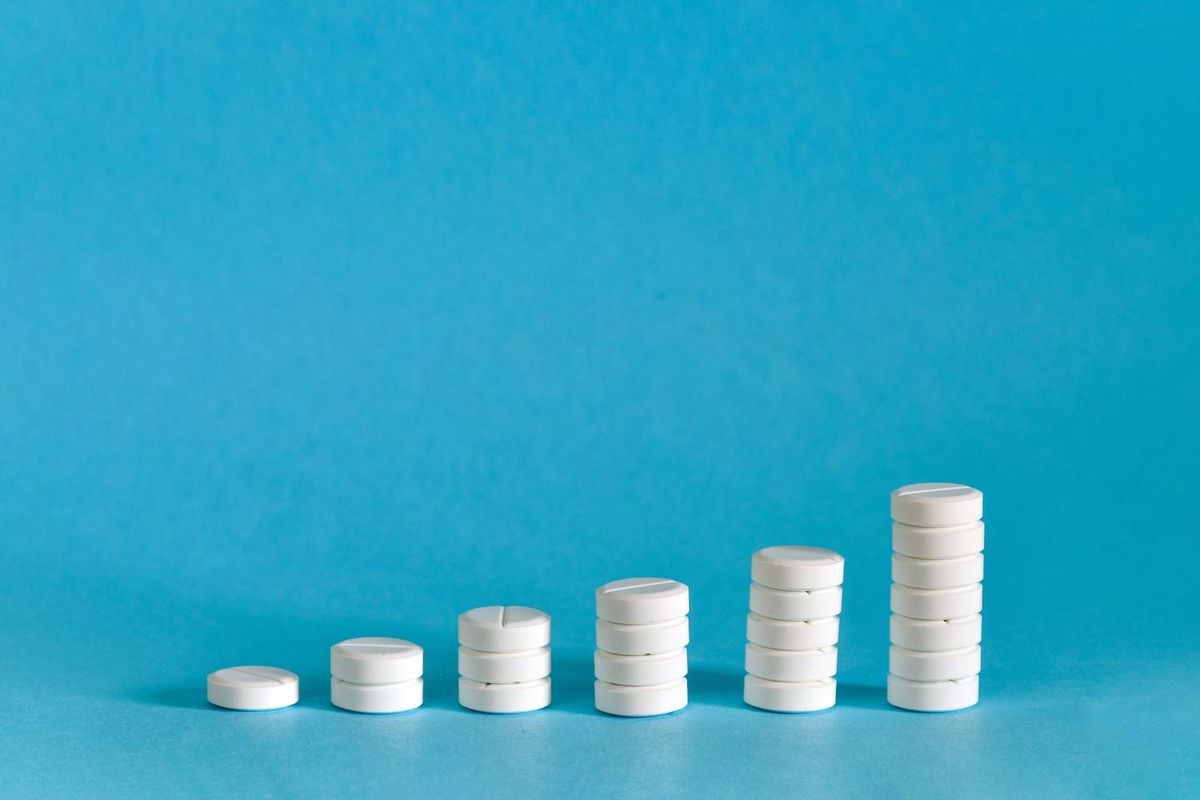 Stacks of white pills progressively increase in height from left to right on a solid blue background.