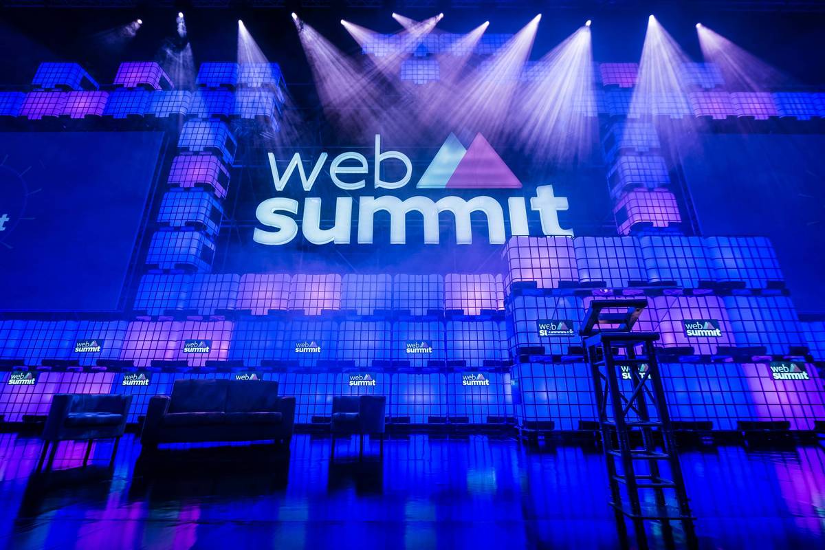 Stage with a purple and blue lit backdrop featuring "web summit" text, with empty chairs and podium below.
