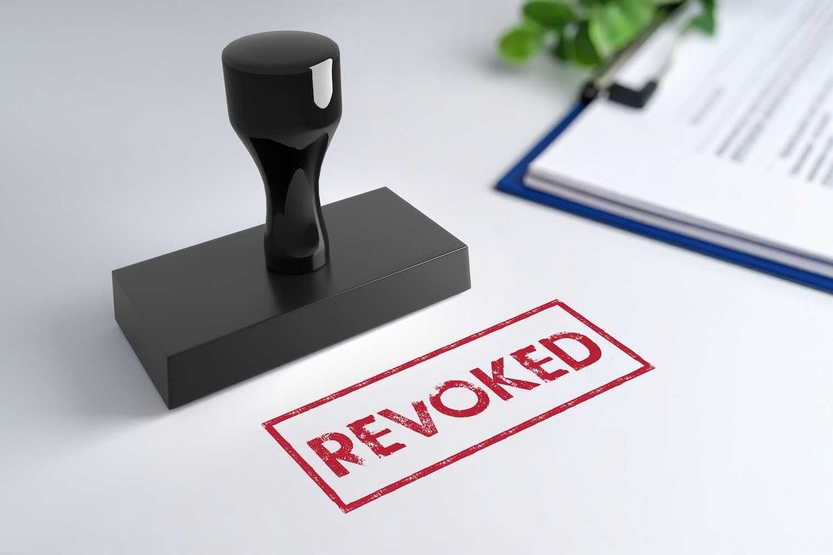 Stamp on white paper with "REVOKED" in red; blurred documents in the background.