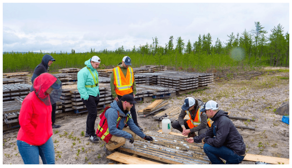 Standard Uranium exploration team examines core samples outdoors near wooded area with stacks of samples behind them.