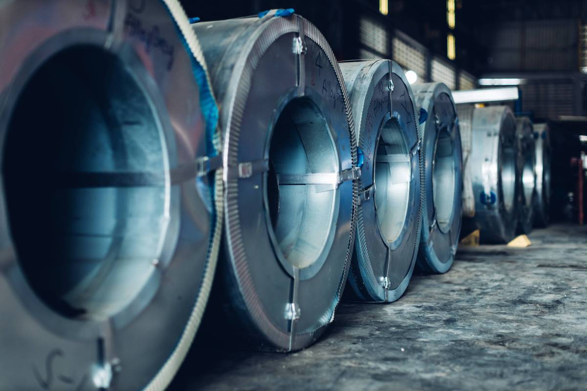 Steel rolls lined up on warehouse floor, with faint text and lighting creating reflections on the surfaces.