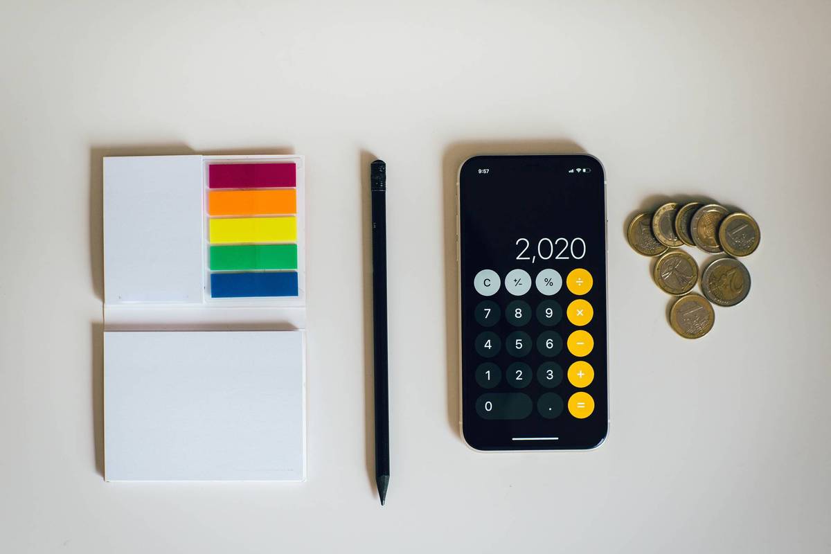Sticky notes, pencil, smartphone calculator and coins on a white surface.