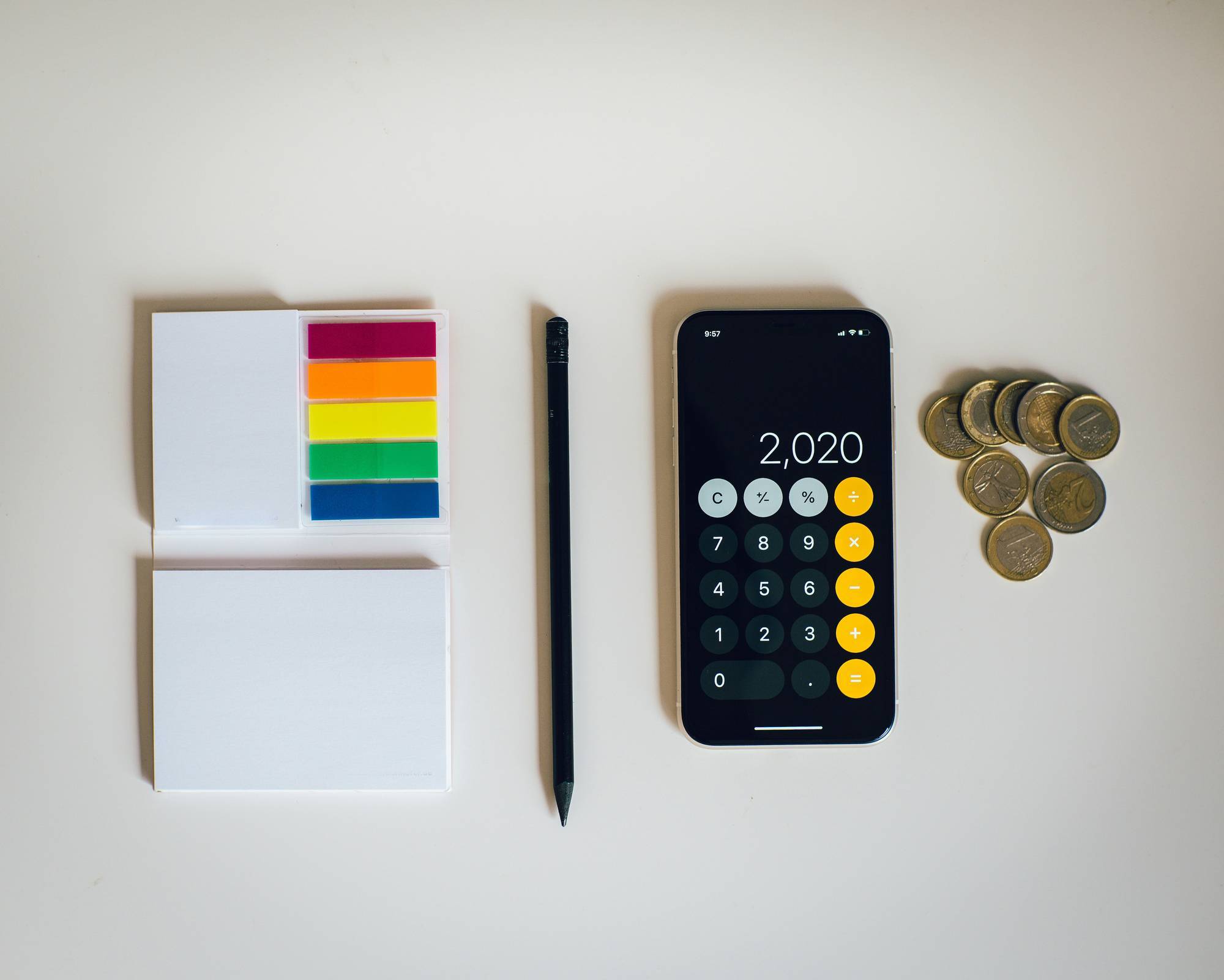 Sticky notes, pencil, smartphone calculator and coins on a white surface.