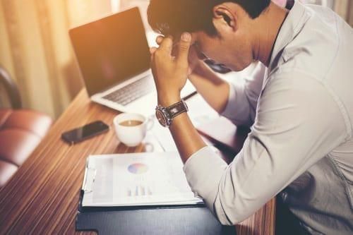 stressed person with head in hands looking at charts on desk