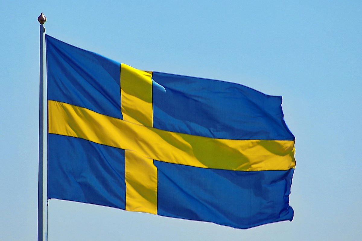 Swedish flag with a yellow cross on a blue background, waving in the clear sky.