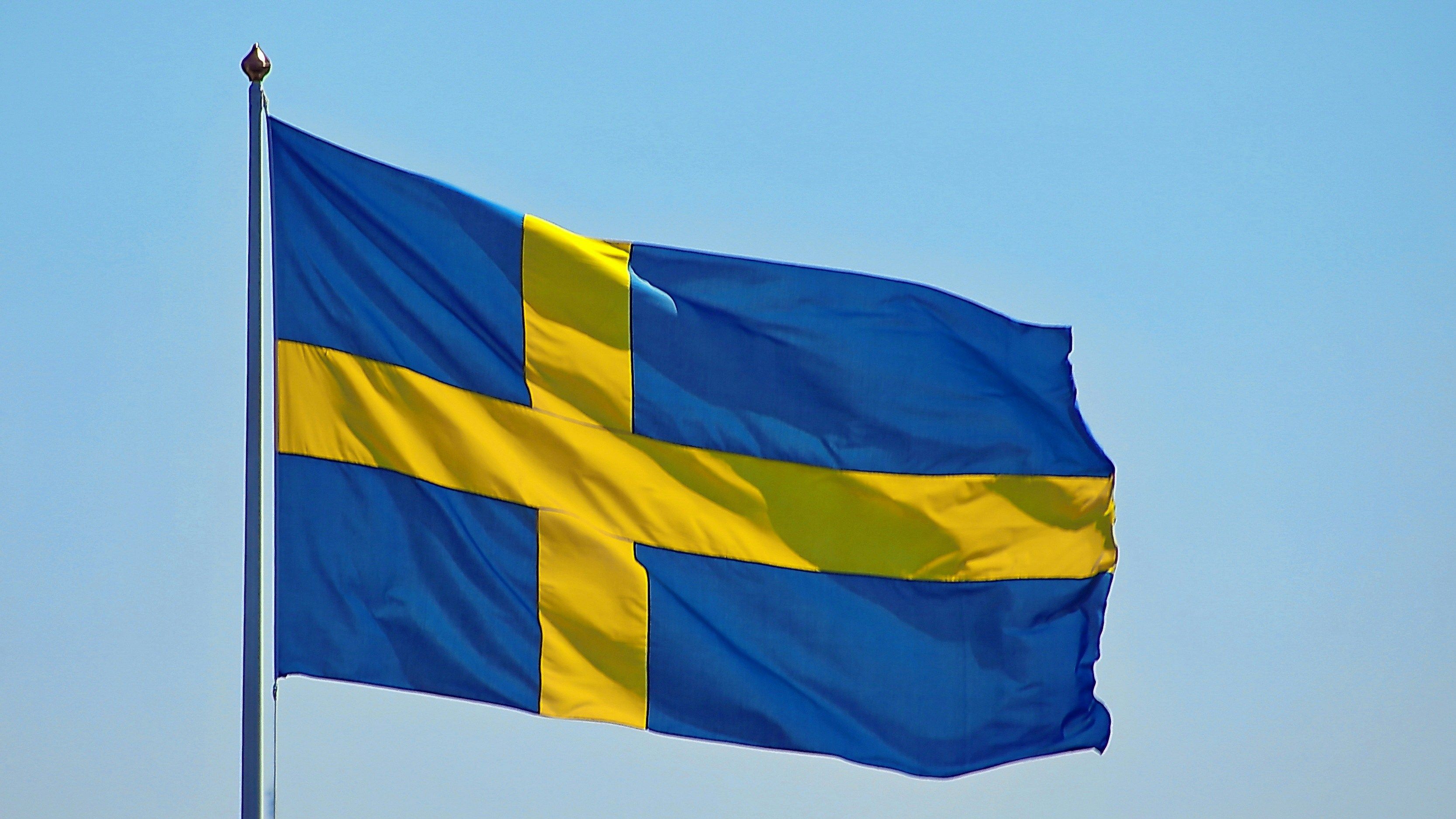 Swedish flag with a yellow cross on a blue background, waving in the clear sky.