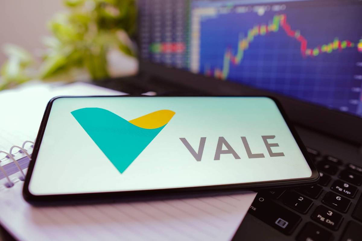 Tablet displaying Vale logo on a laptop, stock market chart in background.