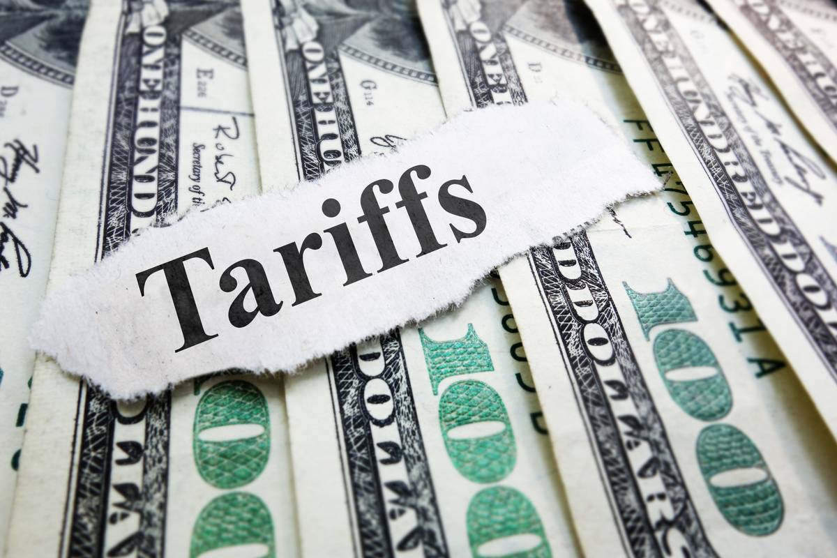 "Tariffs" text on torn paper over stacked US$100 bills.