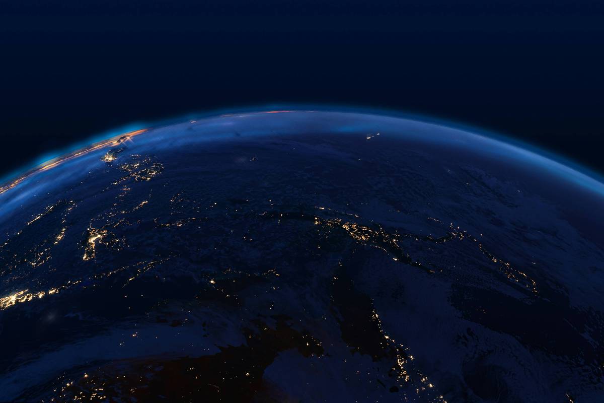 The dark Earth horizon displays glowing city lights under a deep blue sky in a nighttime view from space.