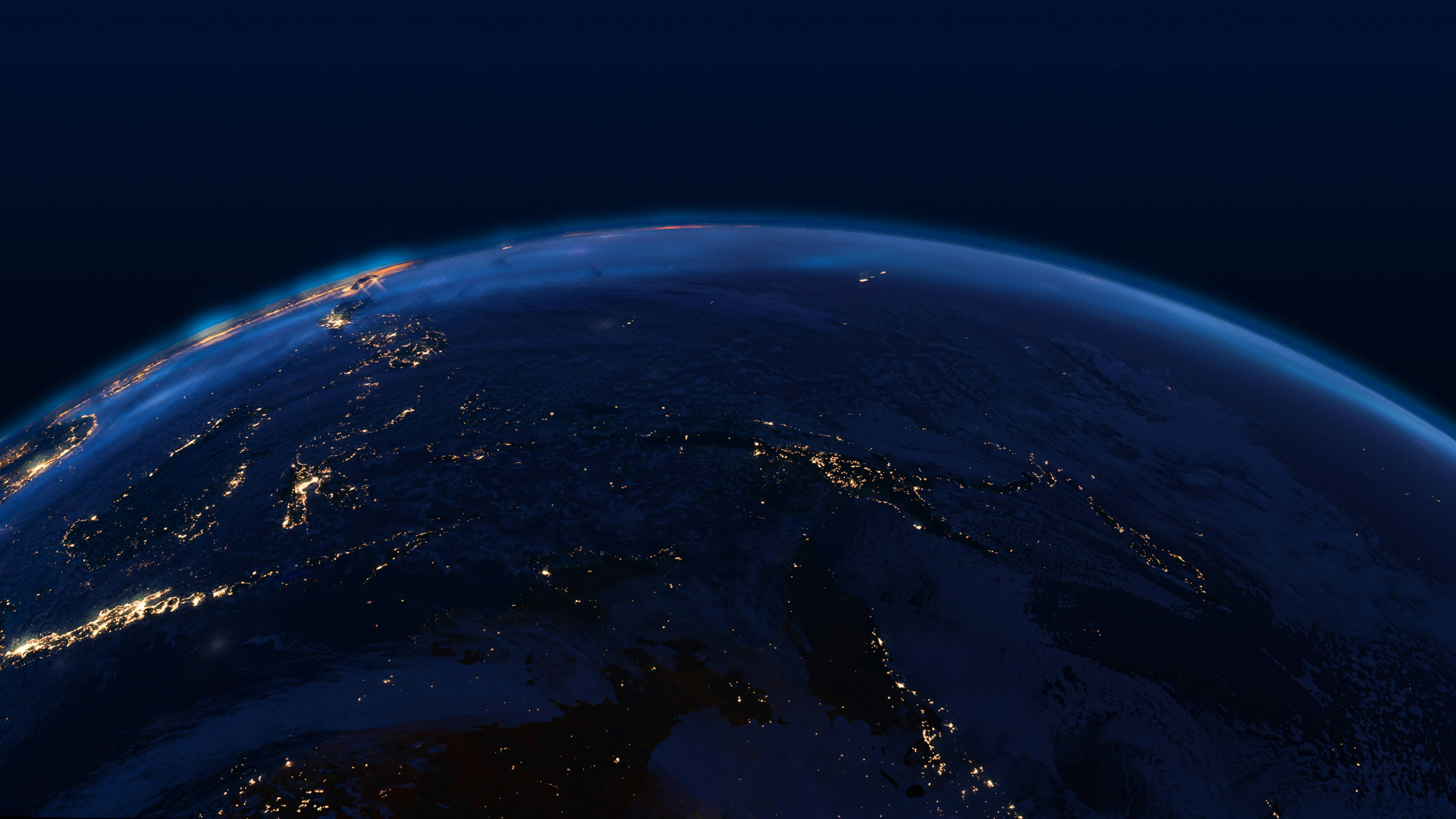 The dark Earth horizon displays glowing city lights under a deep blue sky in a nighttime view from space.