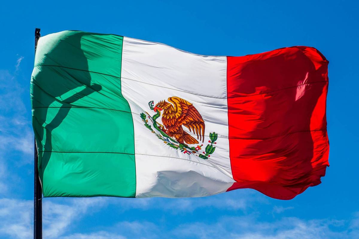 The Mexican flag with green, white, and red stripes waves against a blue sky.