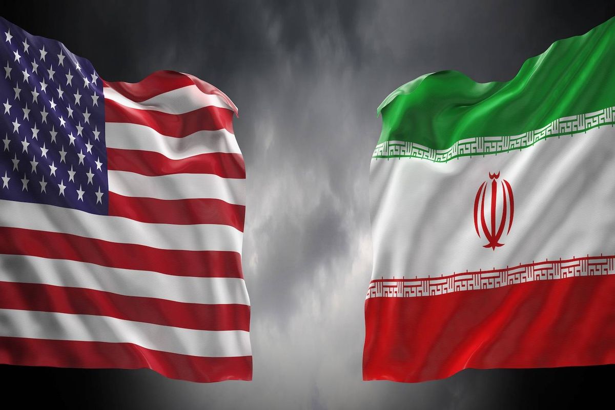 The U.S. and Iranian flags wave against a cloudy, dark gray sky background.