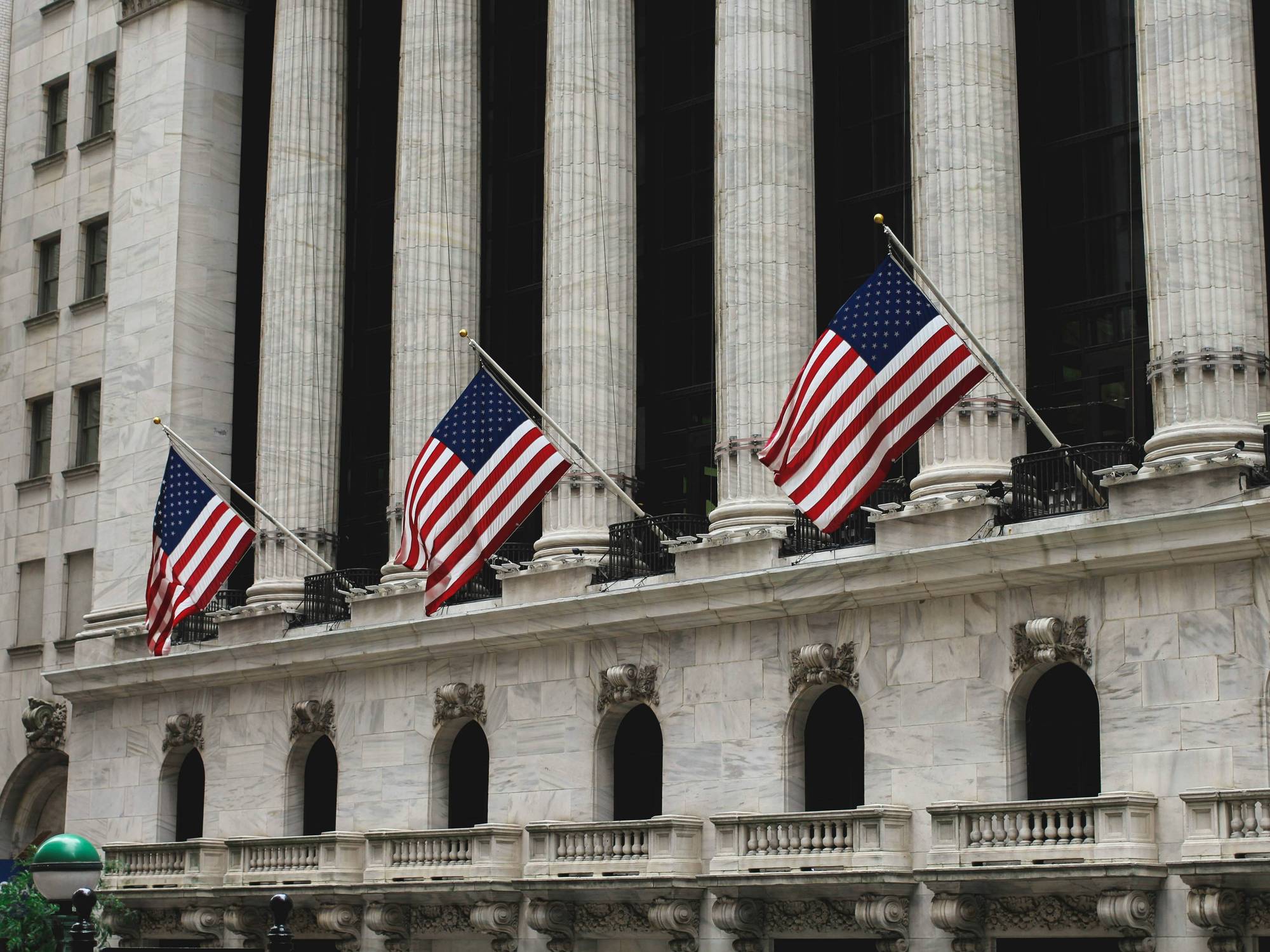 Three American flags hang over a stone building with tall columns and arched windows.