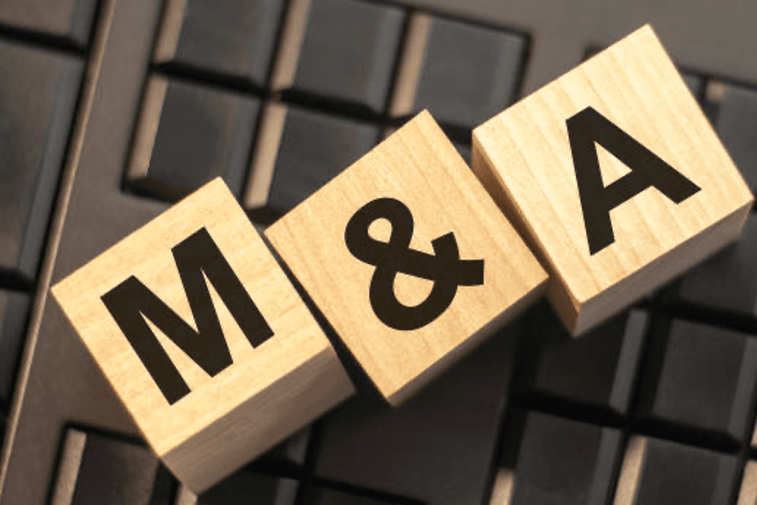 Three wooden blocks with black letters "M&A" rest on a computer keyboard.
