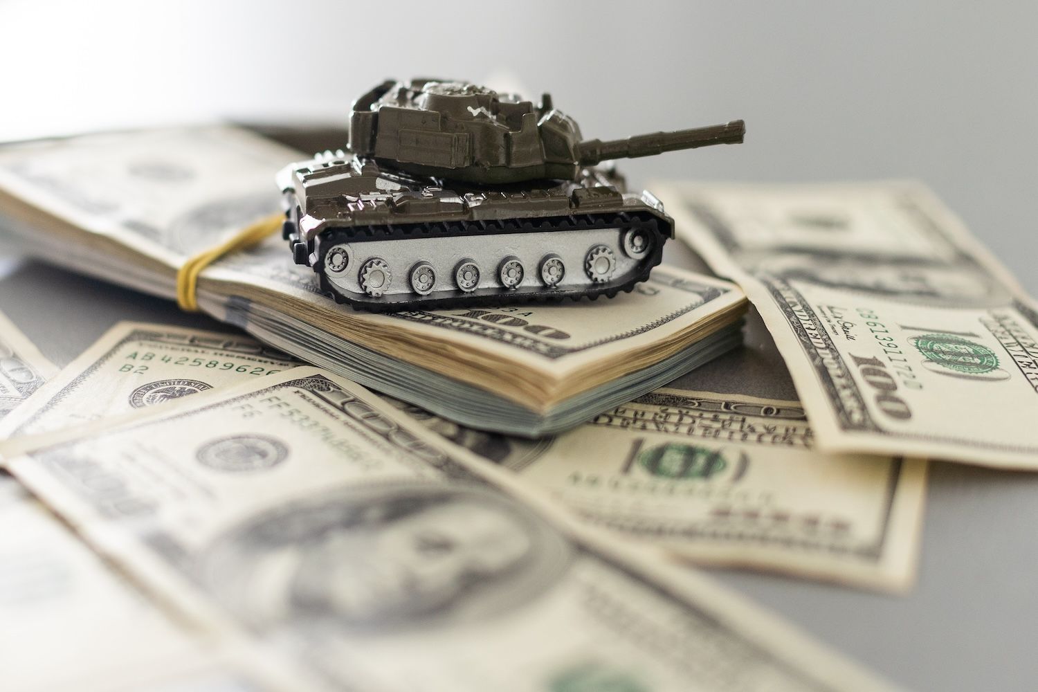 Toy tank on stacked and scattered US dollar bills.