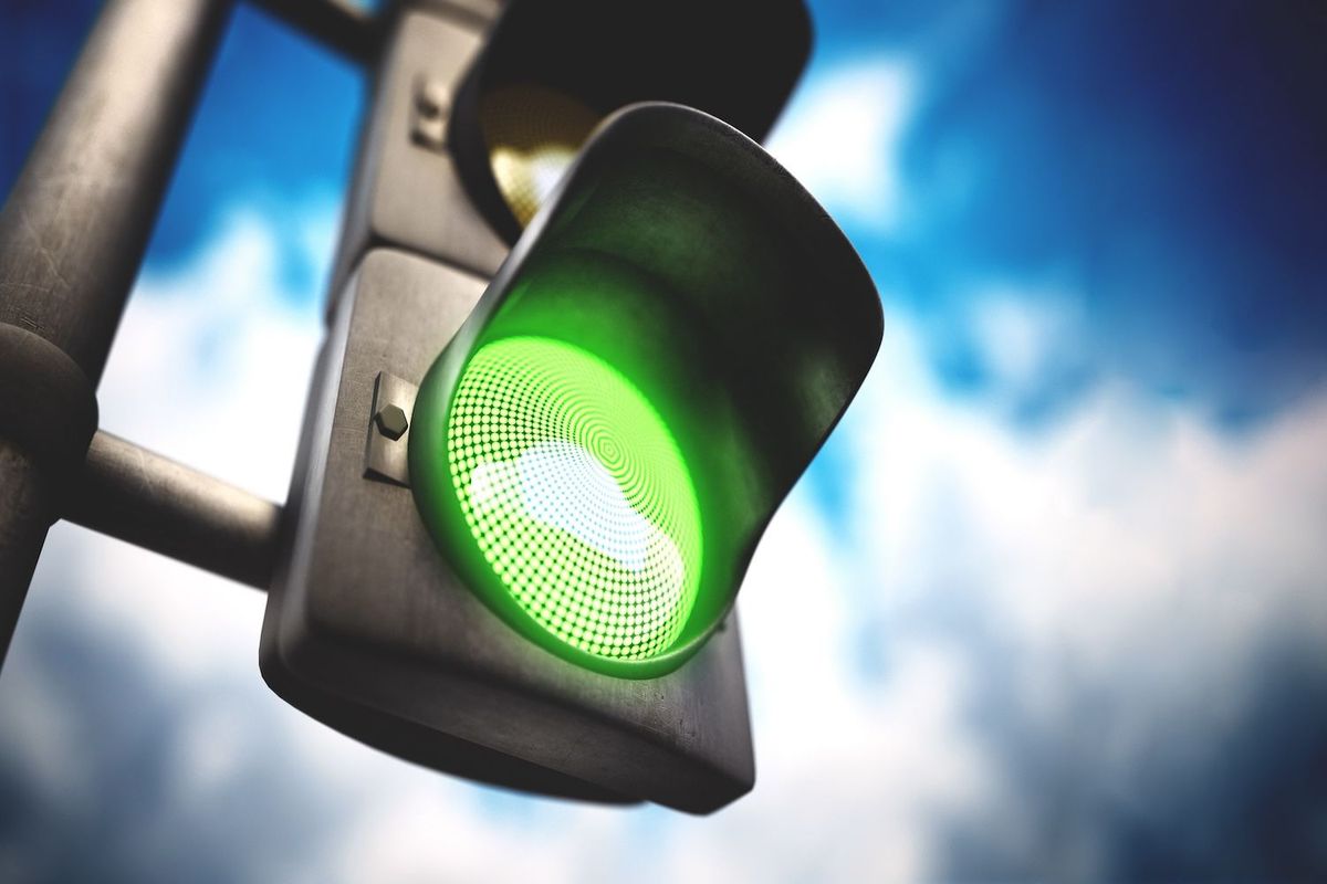 Traffic light showing green against a cloudy blue sky.