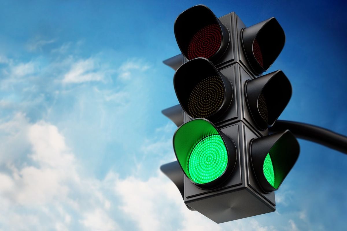 Traffic light with green signal against a cloudy blue sky.