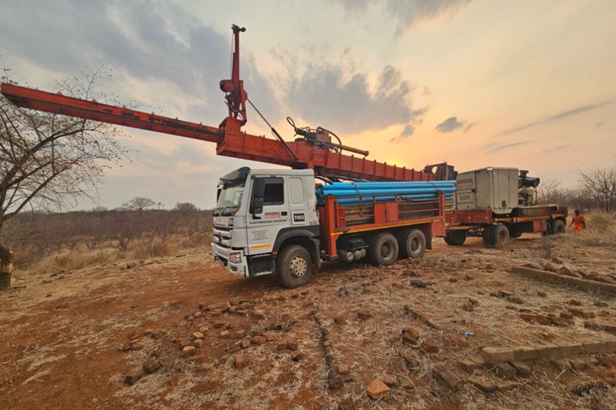 Truck with drill rig at sunset in a dry, grassy landscape.