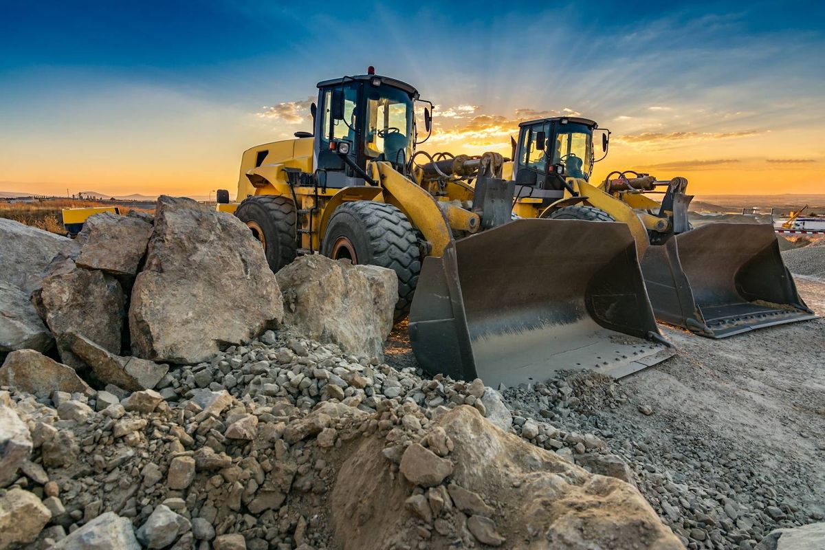 Two bulldozers at a construction site during sunset.