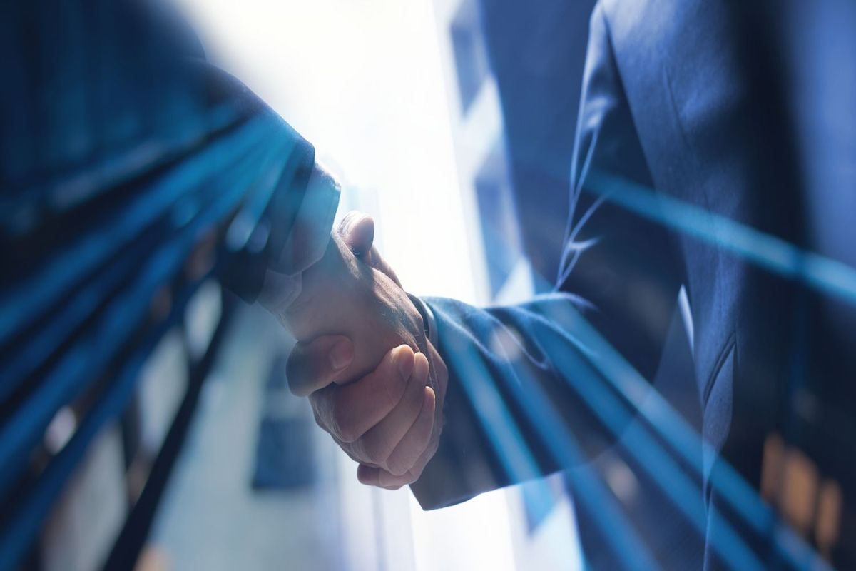 Two businesspeople shake hands amid a blue, abstract background.