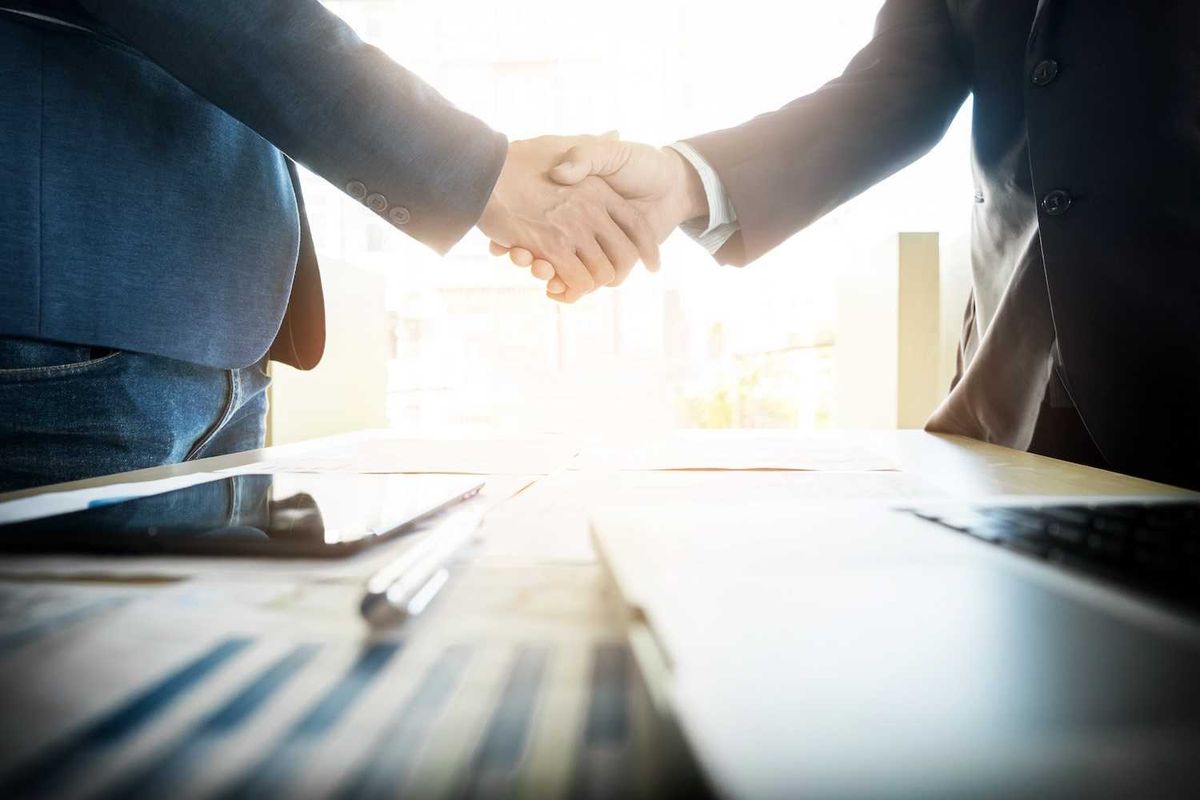 Two businesspeople shaking hands over a desk with documents and a tablet.