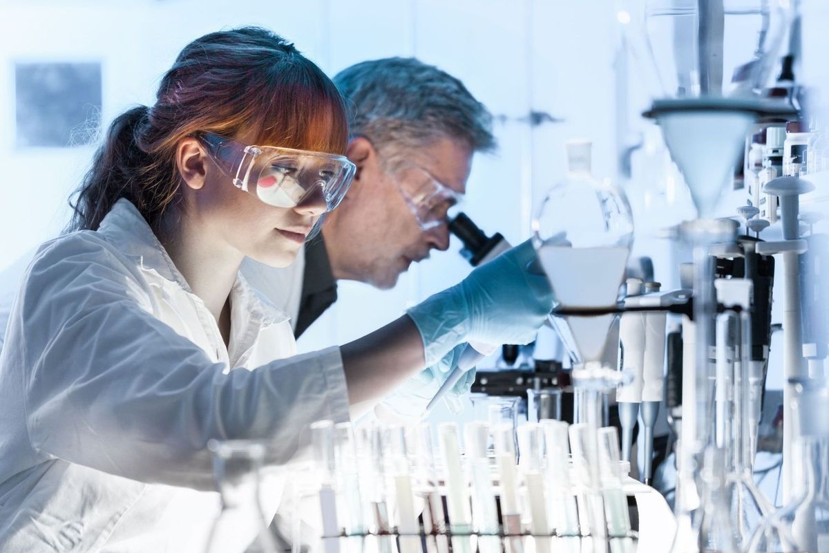 Two life science researchers in a laboratory. One is using a microscope.