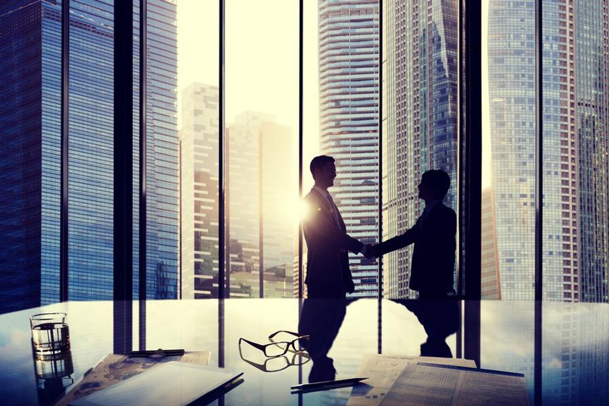 two men shake hands in front of window