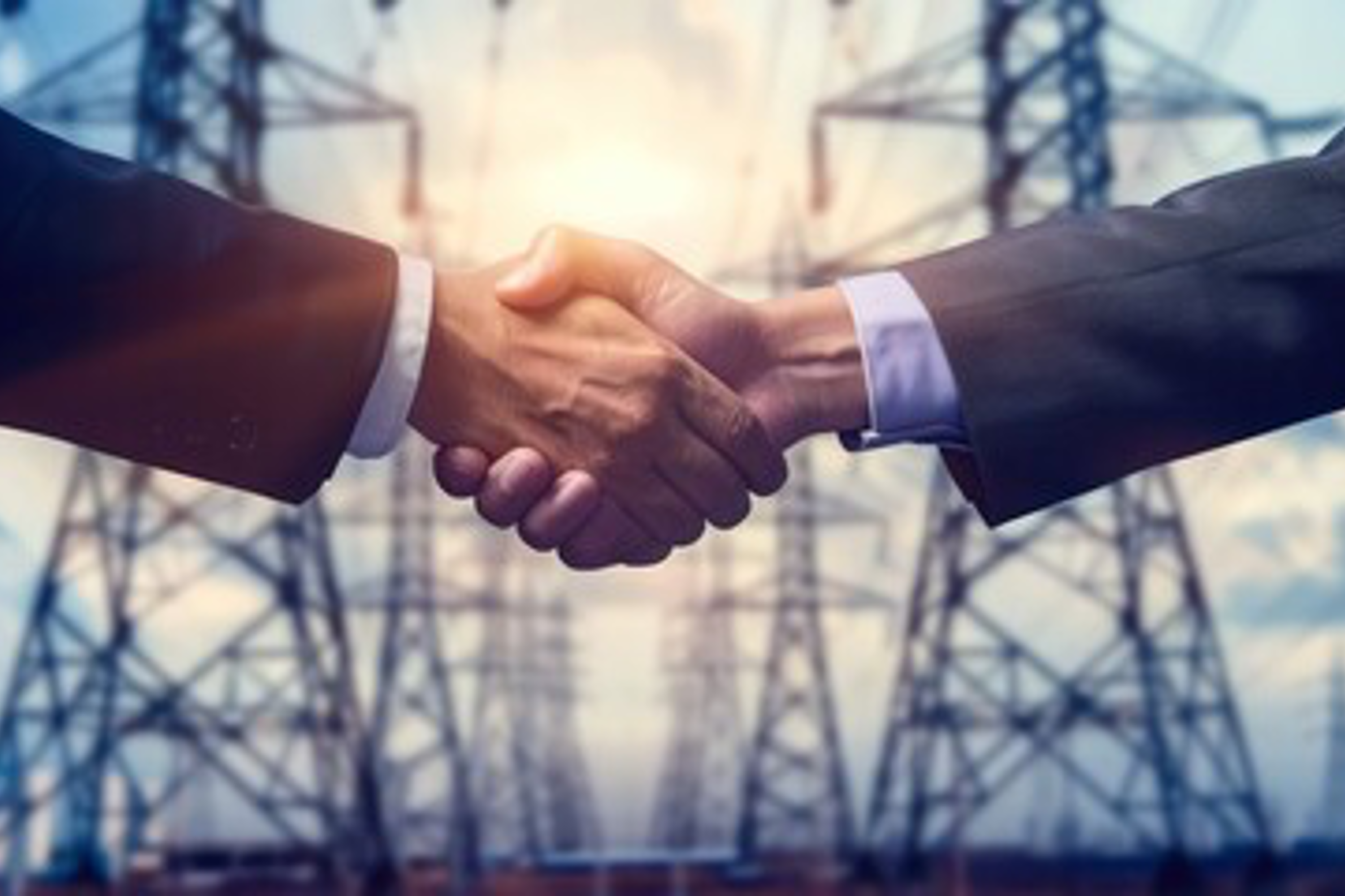 Two men shaking hands in front of electrical towers.