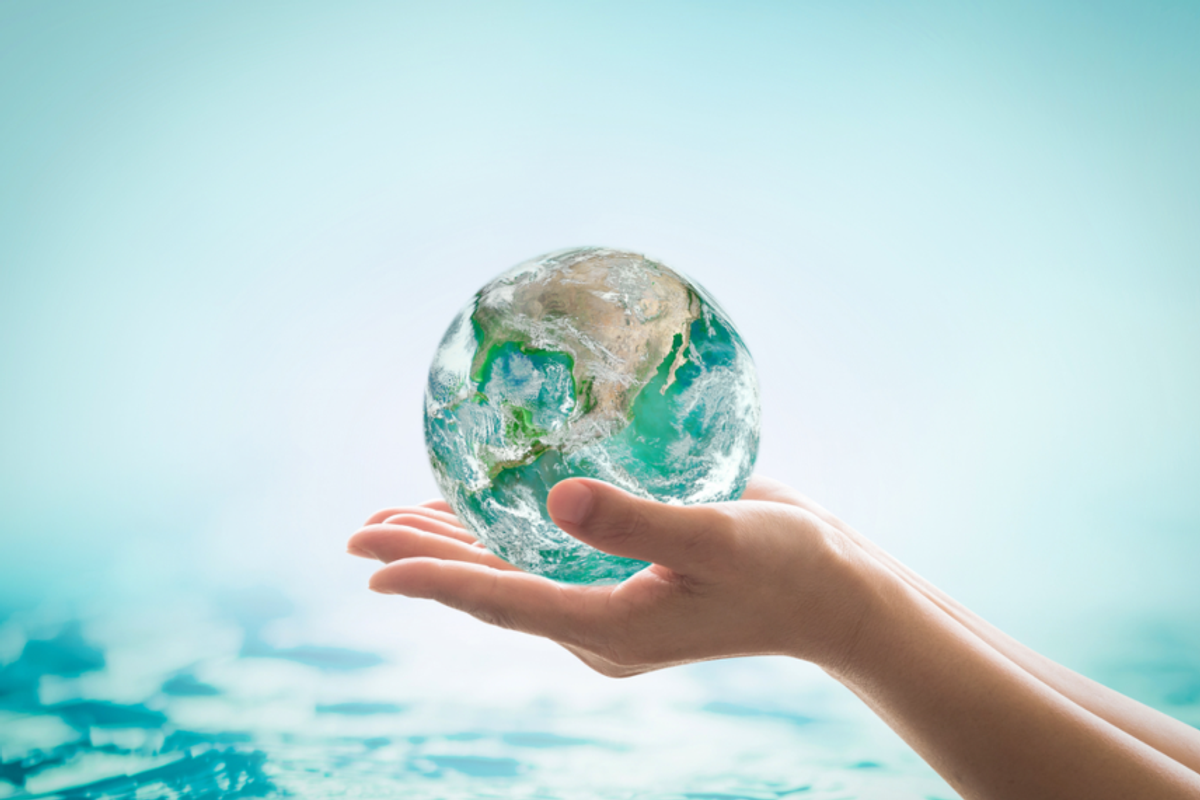 two open palms hold a sphere representing the earth with water in the background