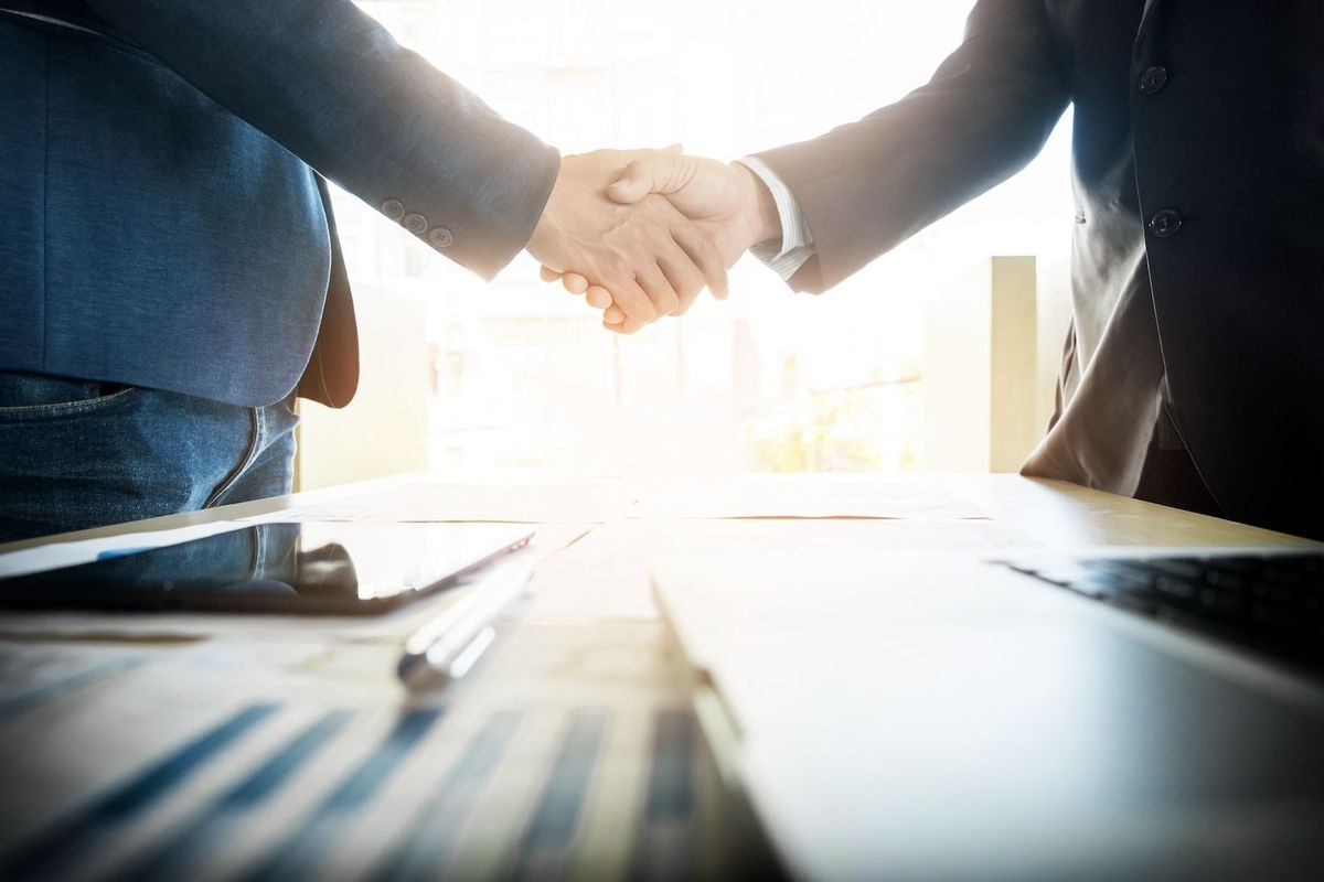 Two people in business attire shaking hands across a table.