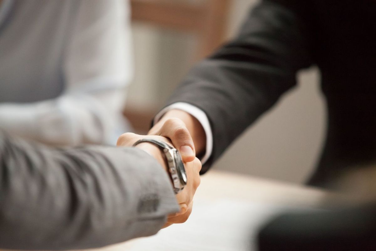 Two people in suits shake hands, agreeing to a deal.