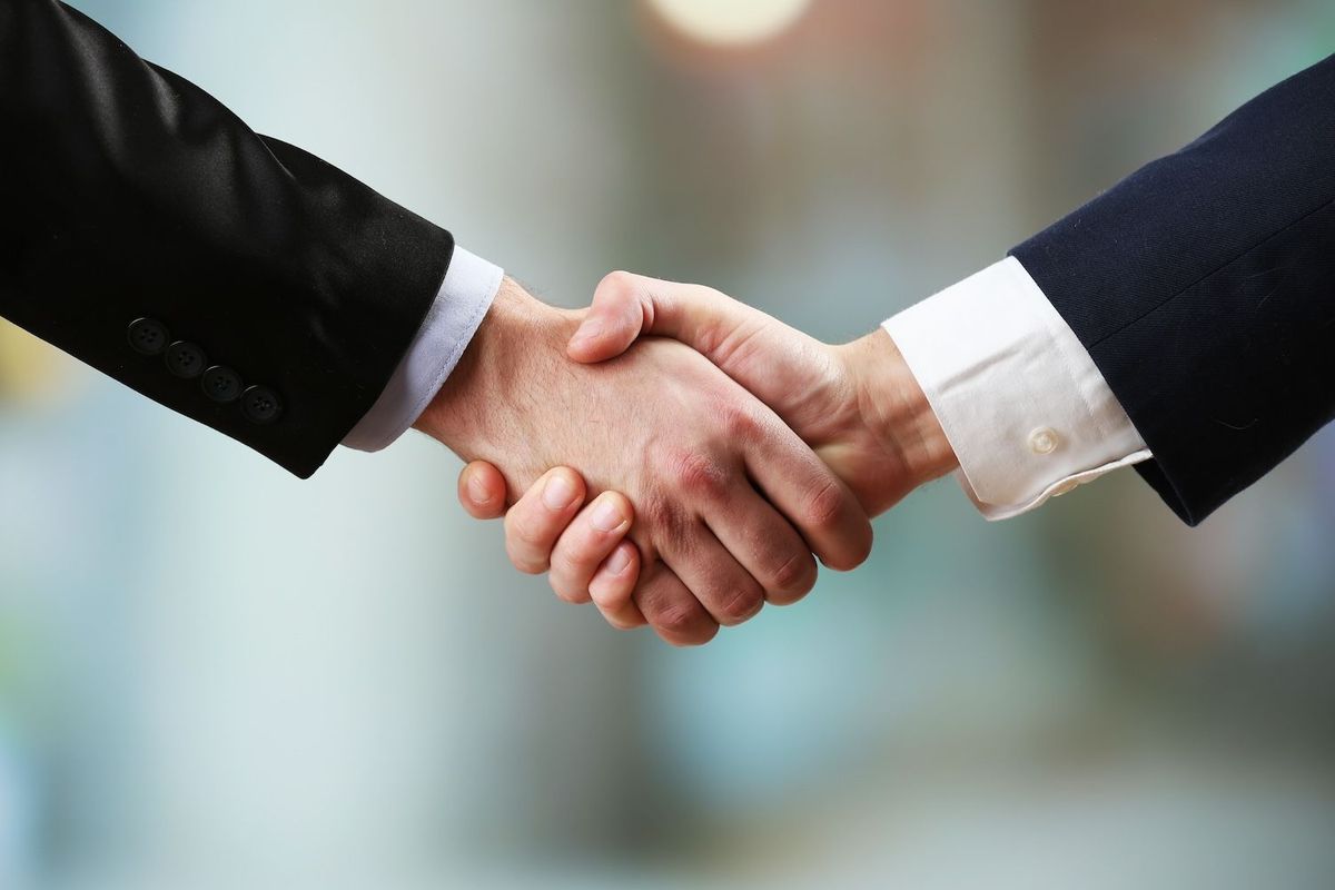 Two people in suits shaking hands, symbolizing agreement or partnership.